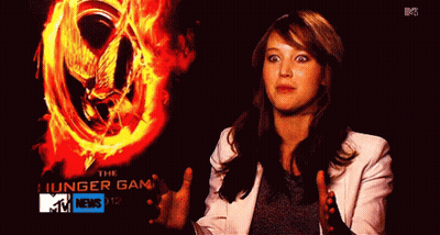 A Woman Standing In Front Of A Poster For The Hunger Games GIF