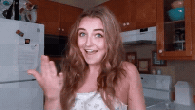 A Woman Standing In Front Of A Refrigerator In A Kitchen Waving Her Hand GIF