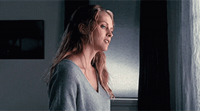 A Woman Standing In Front Of A Window Looking Out GIF
