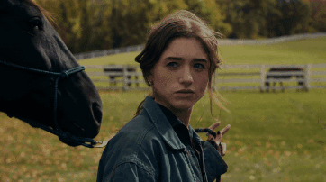 A Woman Standing Next To A Black Horse Looking At The Camera GIF