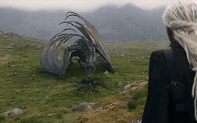 A Woman Standing Next To A Dragon In A Field With Mountains In The Background GIF