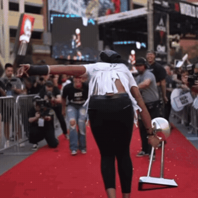A Woman Standing On A Red Carpet Holding A Mirror And A Bottle Of Soda GIF