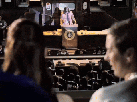 A Woman Stands At A Podium In Front Of A Crowd With A United States Of America Logo GIF