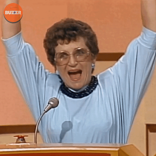 A Woman Stands At A Podium With Her Arms In The Air And A Buzzr Logo Above Her Head GIF