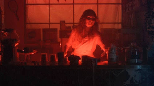 A Woman Stands Behind A Counter In A Dark Room With Purple Lights GIF