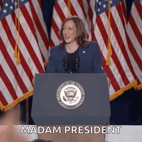 A Woman Stands Behind A Podium With The Words Madam President Written On It GIF