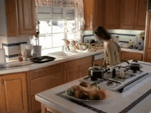 A Woman Stands In A Kitchen With A Plate Of Fruit On The Counter GIF