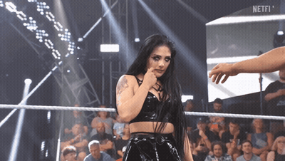 A Woman Stands In A Wrestling Ring With The Word Netfi On The Screen Behind Her GIF