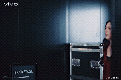 A Woman Stands In Front Of A Backstage Sign GIF