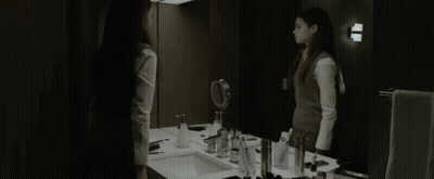 A Woman Stands In Front Of A Bathroom Mirror GIF