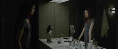 A Woman Stands In Front Of A Bathroom Mirror Looking At Herself GIF