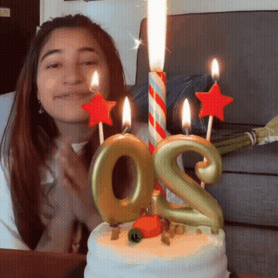A Woman Stands In Front Of A Birthday Cake With Candles In The Shape Of The Number Two GIF