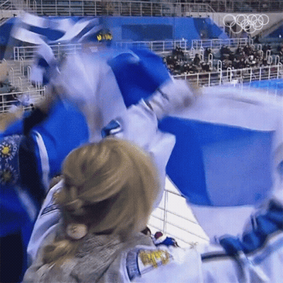 A Woman Stands In Front Of A Blue Box With The Olympic Rings On The Back GIF