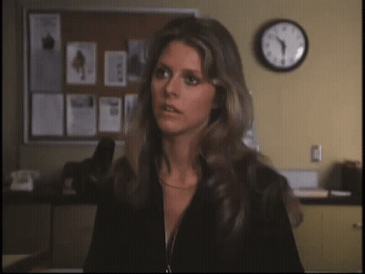 A Woman Stands In Front Of A Bulletin Board With Papers On It And A Clock On The Wall That Shows The Time As 4:20 GIF
