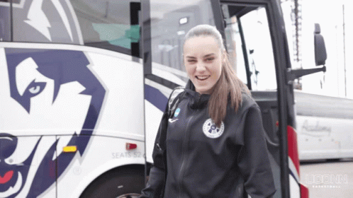 A Woman Stands In Front Of A Bus That Says Seats 52 On It GIF