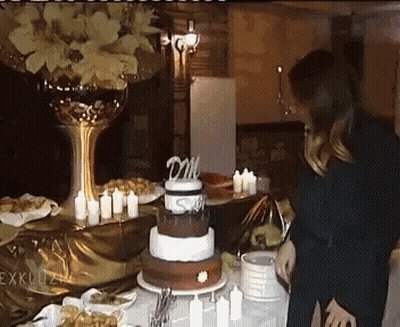 A Woman Stands In Front Of A Cake With A Topper That Says Dm On It GIF