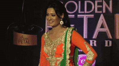 A Woman Stands In Front Of A Golden Petal Advertisement GIF