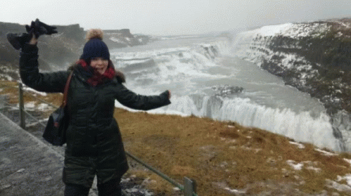 A Woman Stands In Front Of A Large Waterfall GIF