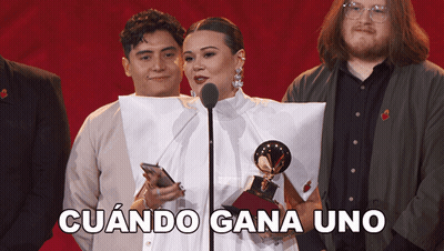 A Woman Stands In Front Of A Microphone Holding A Trophy And The Words Cuando Gana Uno Behind Her GIF