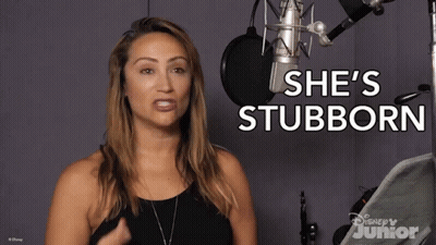 A Woman Stands In Front Of A Microphone With The Words She 'S Stubborn Behind Her GIF