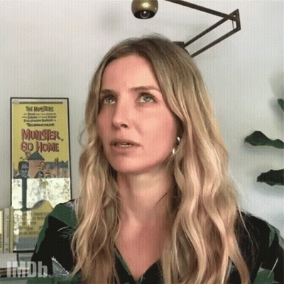 A Woman Stands In Front Of A Poster For The Movie Monster Go Home GIF
