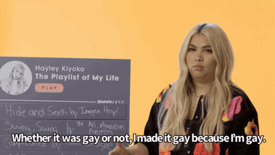 A Woman Stands In Front Of A Sign That Says Hayley Kiyoko The Playlist Of My Life GIF