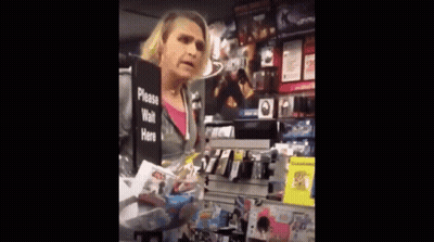 A Woman Stands In Front Of A Sign That Says " Please Wait Here " GIF