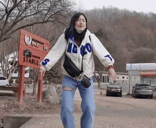 A Woman Stands In Front Of A Sign That Says Stables GIF