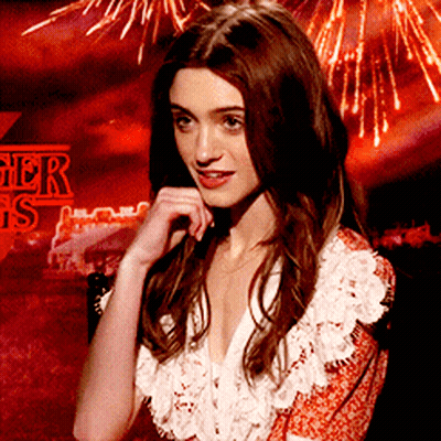 A Woman Stands In Front Of A Sign That Says Stranger Things On It GIF