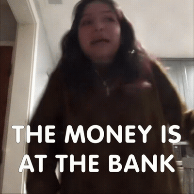 A Woman Stands In Front Of A Sign That Says " The Money Is At The Bank " GIF