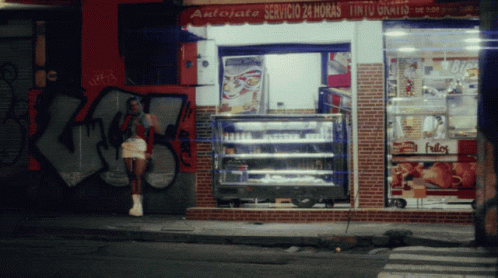 A Woman Stands In Front Of A Store That Says Antojate GIF