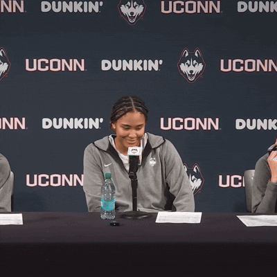 A Woman Stands In Front Of A Uconn Dunk Sign GIF