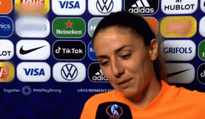 A Woman Stands In Front Of A Wall Of Logos Including Visa And Adidas GIF