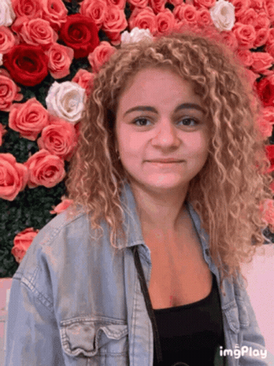 A Woman Stands In Front Of A Wall Of Pink Roses GIF