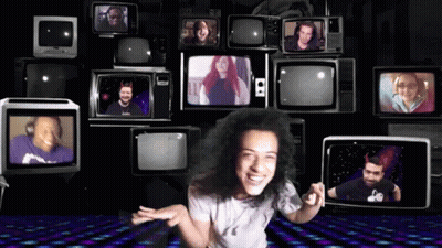A Woman Stands In Front Of A Wall Of Televisions Including One That Says S2 On It GIF