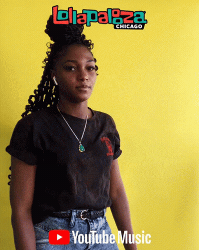 A Woman Stands In Front Of A Yellow Wall With A Lolapaloza Chicago Logo On It GIF