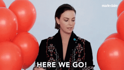 A Woman Stands In Front Of Red Balloons And Says " Here We Go " GIF