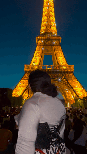 A Woman Stands In Front Of The Eiffel Tower Lit Up At Night GIF