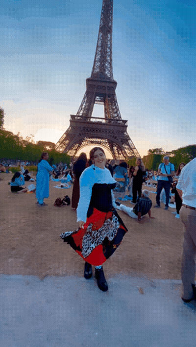A Woman Stands In Front Of The Eiffel Tower Wearing A Leopard Print Skirt GIF