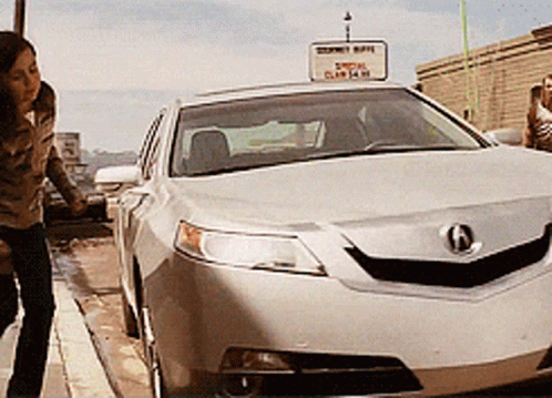 A Woman Stands Next To A Silver Car With A Sign Above It That Says ' Acura ' GIF
