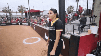 A Woman Stands On A Baseball Field Wearing A Shirt That Says Infinites Unlimited GIF