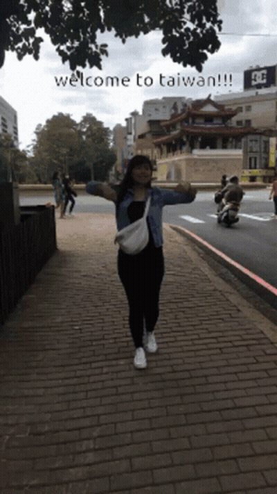 A Woman Stands On A Brick Sidewalk With Her Arms Outstretched And The Words Welcome To Taiwan Written Below Her GIF