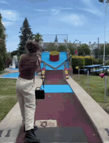 A Woman Stands On A Mini Golf Course With A Purse GIF