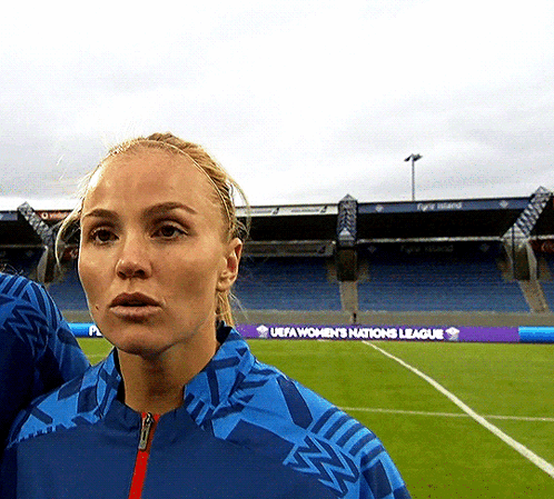 A Woman Stands On A Soccer Field With A Uefa Women 'S Nations League Banner In The Background GIF