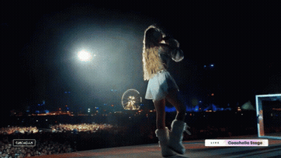 A Woman Stands On A Stage In Front Of A Crowd With A Sign That Says Coachella Stage GIF