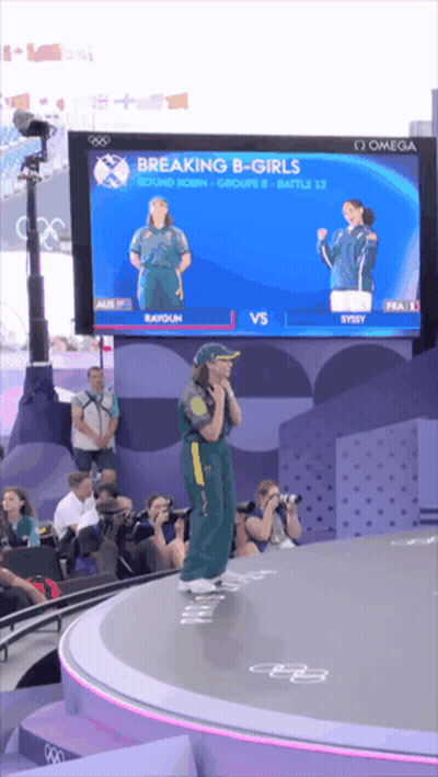 A Woman Stands On A Stage In Front Of A Large Screen Which Says Breaking B-Girls GIF