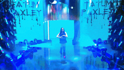 a woman stands on a stage in front of a wall that says tatum oakley