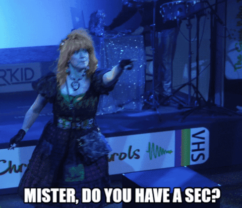 A Woman Stands On A Stage With A Sign That Says Vhs GIF