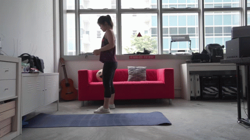 A Woman Stands On A Yoga Mat In Front Of A Red Couch And A Sign That Says Walk On The Side GIF