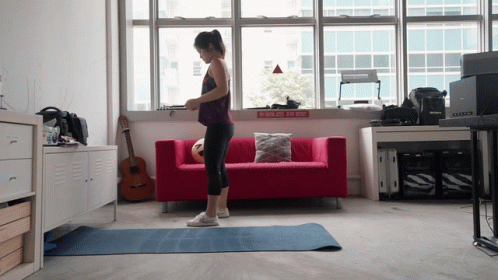 A Woman Stands On A Yoga Mat In Front Of A Red Couch With A Sign That Says " Do Not Enter " GIF